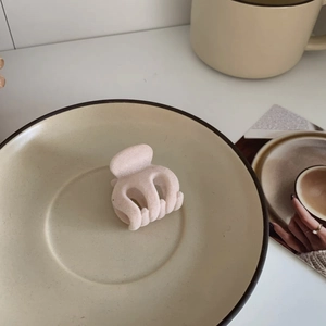 Close-up of a small beige velvet hair claw clip in a ceramic dish with artistic props