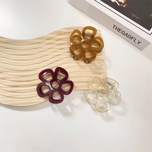 Tre pinze per capelli a fiore nei colori marrone, rosso e trasparente su legno