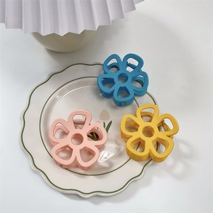 Detailed close-up of matte flower-shaped hair claws in pink, blue, and yellow on a ceramic plate