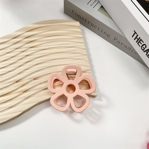 Detail of pink hollow floral hair claw clip on wooden wave board with matte finish