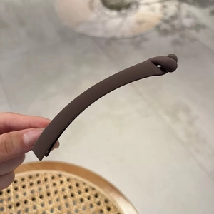 Detail of matte dark coffee hair clip featuring a minimalist knot design and sleek arc shape