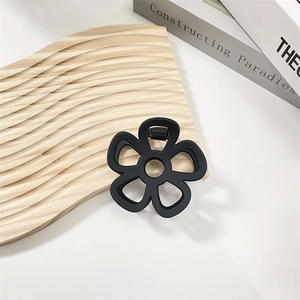 Close-up of black matte flower hair claw clip with metal spring on wooden surface