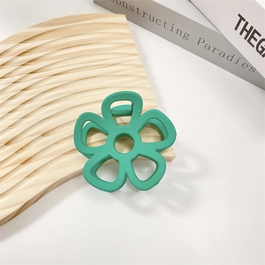 Close-up of a matte green hollow flower hair claw clip on a wavy wooden board
