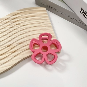 Detailed top view of a matte pink flower claw clip on a wavy wooden display board