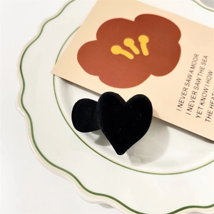 Close-up of black flocked heart hair claw with velvet texture on a decorative ceramic plate