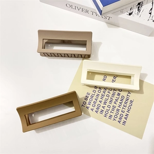 Three matte rectangular hair claws in brown, cream and khaki gray on a book