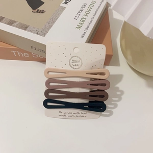 Close-up of four matte oval hair clips in muted tones on a branded display card