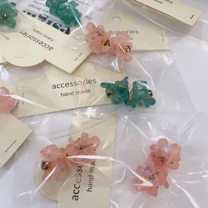 Détail de barrettes camélia en résine rose et verte avec strass en centre sous emballage