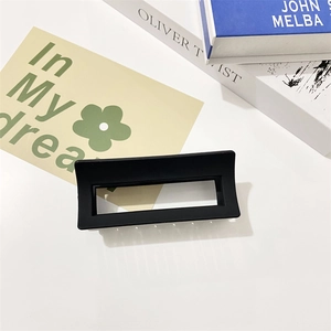 Detail of a large matte black rectangular hollow hair claw clip on a white table