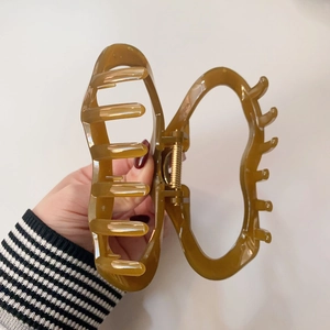 Makro-Detail einer großen bernsteinbraunen Haarklammer aus Harz mit goldener Metallfeder