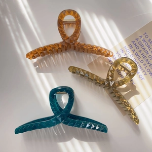 Detail of three large translucent hair claws with geometric facets under striped lighting