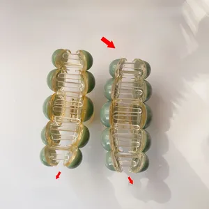 Detail view comparing thickness of acrylic hair claw clips with green translucent beads