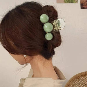 Macro detail of large acrylic hair claw clip with green beads on model's wavy hair