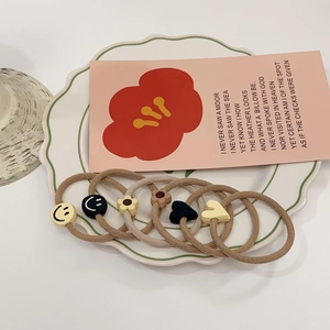 Detail of high-elastic hair ties with matte smile, flower, and heart charms in a ceramic dish