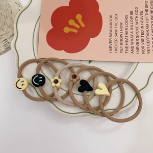 Detailed close-up of 6 elastic hair ties with cute smile and heart charms in a ceramic bowl