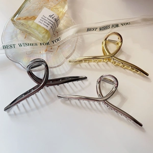 Three metallic hair claw clips in gold silver and gun black shown on a textured tabletop