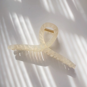 Macro detail of geometric textured cream hair claw with metallic gold spring and light shadows