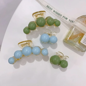 Close-up of pearl acrylic hair claws in green and blue colors with elegant packaging