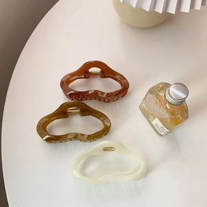 Drei elegante Haarspangen in Braun, Oliv und Creme in Wellenform auf weißem Tisch