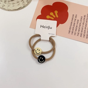 Detail view of two light brown elastic hair ties with yellow and black smiley face charms