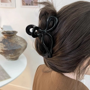 Detail of elegant black glossy bow hair claw clip styled on a woman's brown hair bun