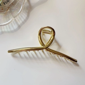 Detail of large gold metal hair claw clip with minimalist twist design and secure teeth