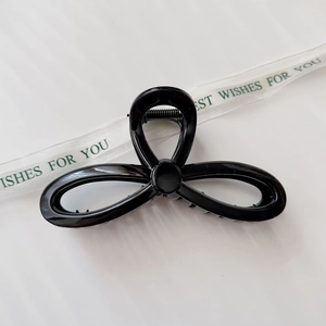 Close-up of a large black glossy hair claw clip with a sleek clover-shaped design on silk