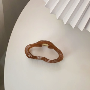 Große bernsteinfarbene Haarklammer mit goldener Metallfeder auf einem minimalistischen Ständer