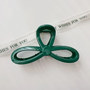 Macro view of a large dark green hair claw clip with a glossy triple-loop woven design