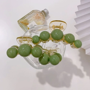 Detail of light yellow resin hair claw with olive green spherical ornaments on glass