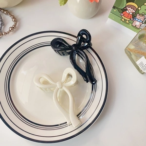 Pair of black and cream jelly bow hair claws on a stylish ceramic plate background