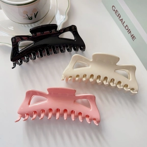 Détail de trois grandes pinces à cheveux évidées en noir, crème et rose pour cheveux épais