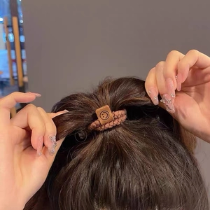 Close-up of brown braided hair tie with square leather smiley face tag on ponytail