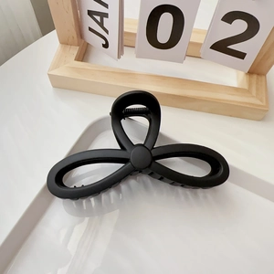 Close-up of a matte black flower-shaped hair claw clip on a minimalist white tray