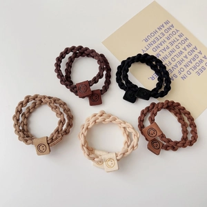 Detail of five elastic braided hair ties in earth tones with leather smiley face charms