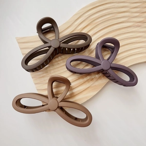 Three large matte flower claw clips in earth tones displayed on a textured wooden tray