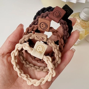 Detail of four high-elasticity braided hair ties in earthy tones with square smiley tags