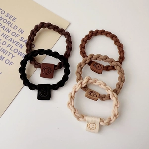 Detail of five elastic hair ties in earth tones featuring a square smiley face charm