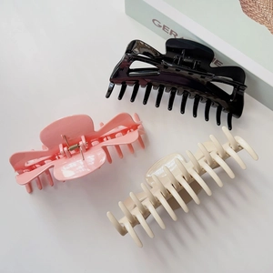 Trois grandes pinces à cheveux noires, roses et crème sur fond de magazine de mode