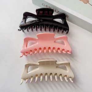 Vue à plat de grandes pinces à cheveux crème, noires et roses sur fond blanc épuré