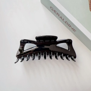 Grande pince à cheveux noire brillante montrant les dents de préhension et la texture polie