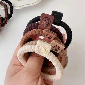 Close-up of durable woven elastic hair ties with a minimalist leather smiley face tag