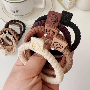 Close-up of braided elastic hair ties in earth tones with stitched smiley face leather tags
