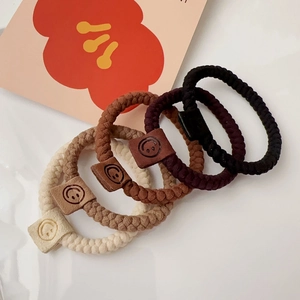 Detail of high-elastic braided hair ties in earth tones with embossed smiley face tags