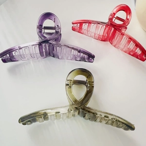 Detailed view of three large transparent hair claw clips in purple red and grey-green colors