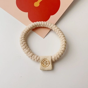 Detail of beige braided elastic hair tie featuring a yellow square smiley face charm