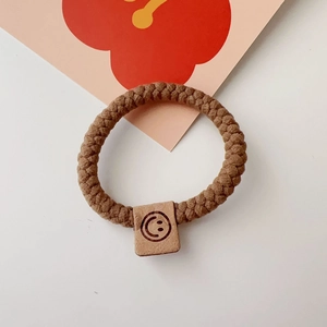 Close-up of brown braided elastic hair tie with a square black smiley face charm detail