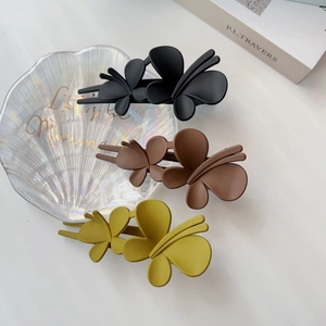 Trois pinces à cheveux papillon mates en noir, cacao et jaune sur un plateau coquillage