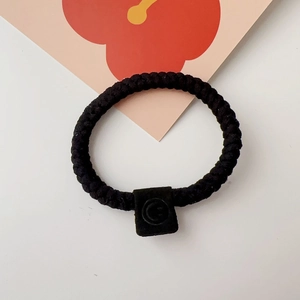 Close-up of thick black braided hair tie with a textured matte square decorative buckle