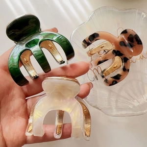 Detailed view of three resin hair claws in emerald green, tortoise, and pearly white finishes